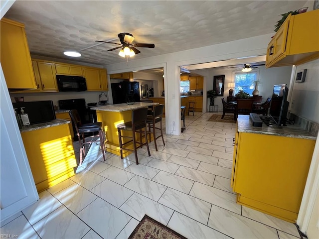 kitchen with a center island, marble finish floor, a breakfast bar area, ceiling fan, and black appliances