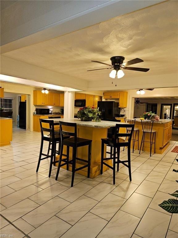 kitchen featuring ceiling fan, a peninsula, light countertops, black appliances, and a kitchen bar