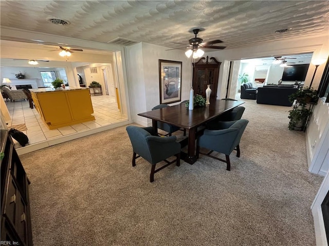 dining space with light carpet, ceiling fan, a fireplace, and visible vents