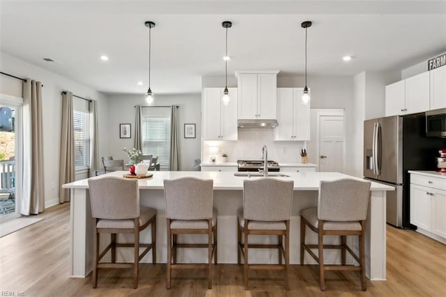 kitchen with appliances with stainless steel finishes, a kitchen island with sink, light countertops, under cabinet range hood, and a sink