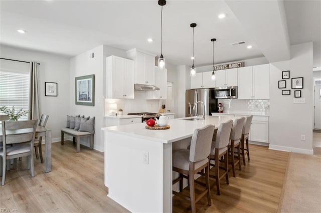 kitchen featuring a kitchen island with sink, under cabinet range hood, stainless steel appliances, visible vents, and light countertops