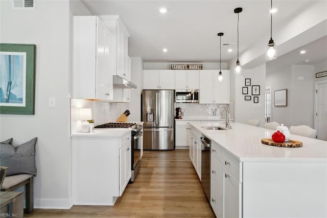 kitchen with stainless steel appliances, light countertops, white cabinetry, a sink, and under cabinet range hood