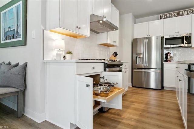 kitchen with white cabinets, appliances with stainless steel finishes, light wood-type flooring, under cabinet range hood, and backsplash