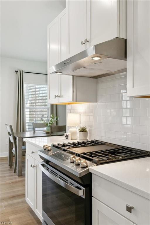 kitchen featuring stainless steel gas stove, white cabinets, light countertops, light wood-style floors, and backsplash