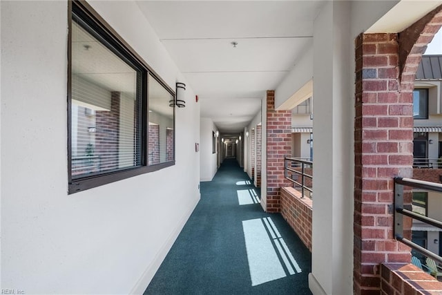 hall featuring brick wall, baseboards, and carpet flooring