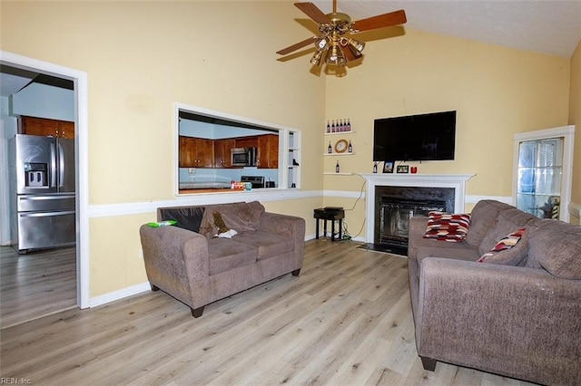 living area featuring a ceiling fan, a fireplace with flush hearth, high vaulted ceiling, and wood finished floors