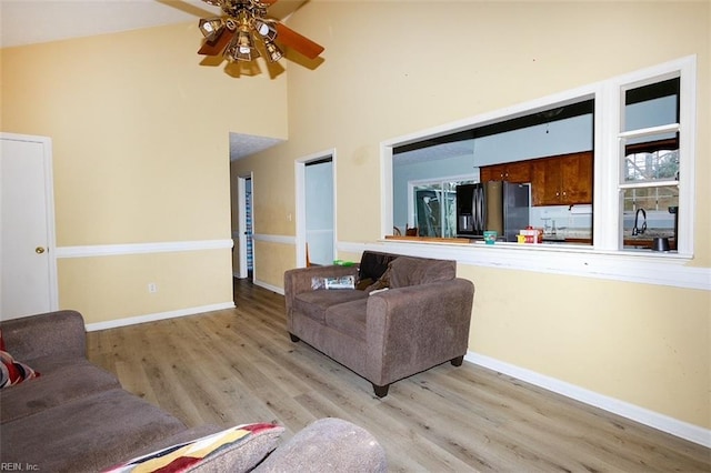 living room featuring ceiling fan, a towering ceiling, baseboards, and wood finished floors