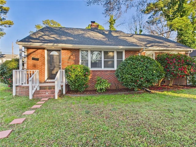 view of front of property featuring roof with shingles, brick siding, a front lawn, and a chimney