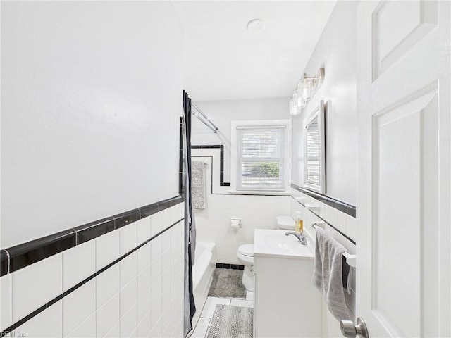 bathroom featuring tile patterned flooring, toilet, a wainscoted wall, vanity, and tile walls