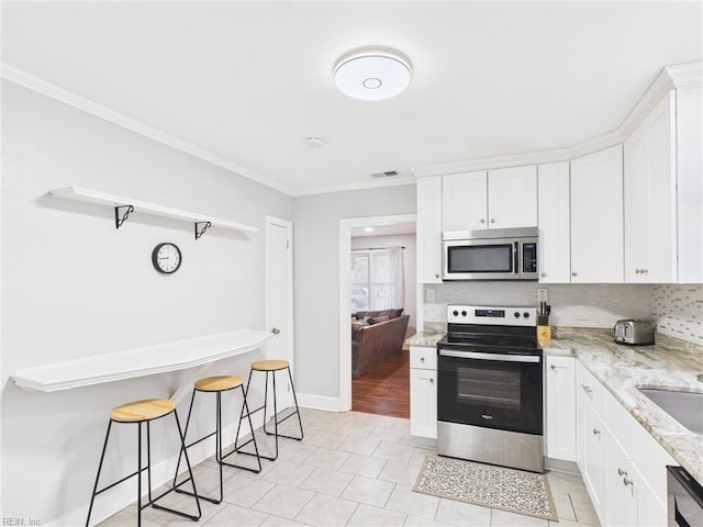 kitchen with visible vents, white cabinets, ornamental molding, light stone countertops, and stainless steel appliances