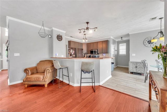 kitchen featuring visible vents, a breakfast bar area, hanging light fixtures, stainless steel appliances, and light wood-type flooring