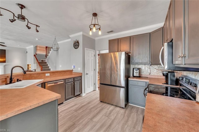 kitchen featuring stainless steel appliances, light countertops, backsplash, ornamental molding, and a sink