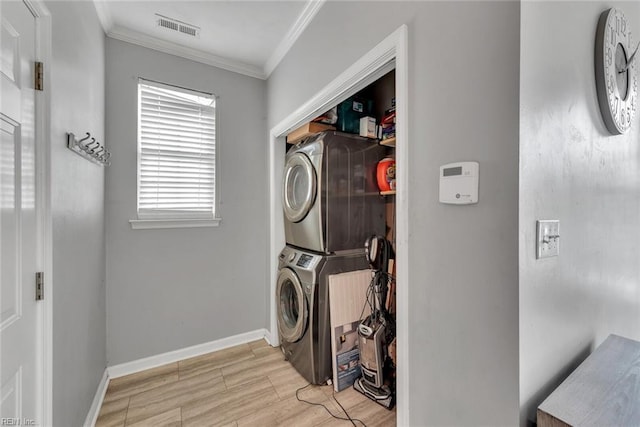 clothes washing area featuring crown molding, stacked washer / drying machine, visible vents, laundry area, and baseboards