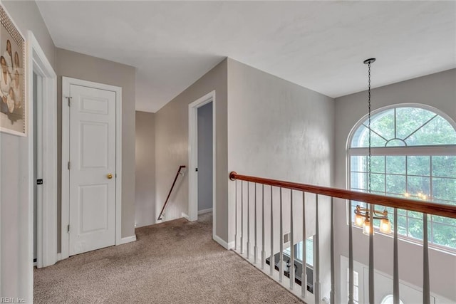 corridor featuring carpet, baseboards, a notable chandelier, and an upstairs landing