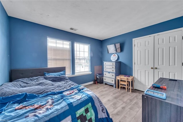 bedroom with light wood-type flooring, baseboards, visible vents, and a closet