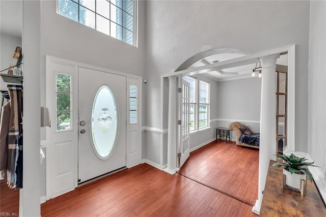 foyer entrance featuring arched walkways, decorative columns, a towering ceiling, and hardwood / wood-style flooring