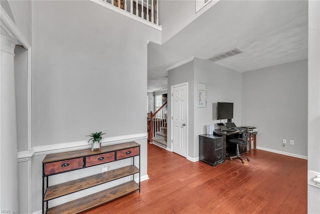 office area with ornate columns, wood finished floors, visible vents, and baseboards