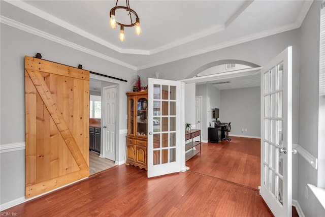 spare room with arched walkways, a barn door, wood finished floors, french doors, and a tray ceiling