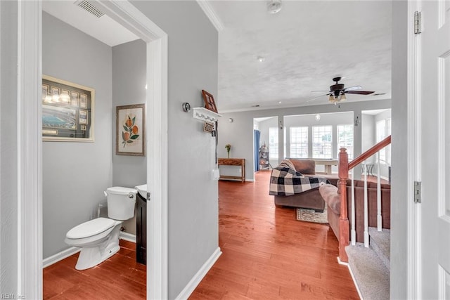 hall with visible vents, ornamental molding, wood finished floors, baseboards, and stairs