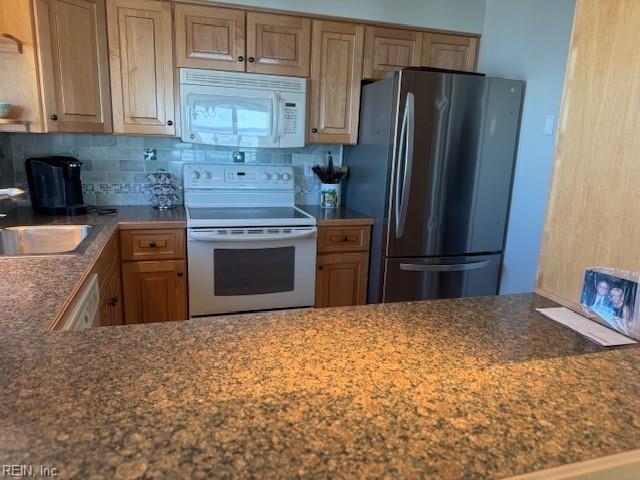 kitchen featuring dark countertops, decorative backsplash, white appliances, and a sink