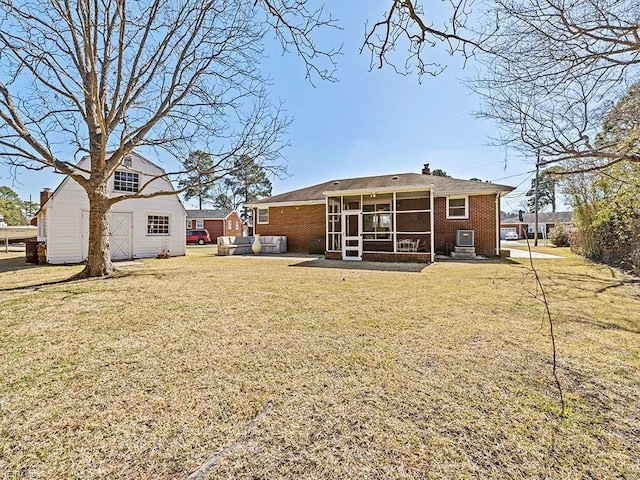 back of property featuring an outbuilding, brick siding, a yard, a chimney, and a sunroom