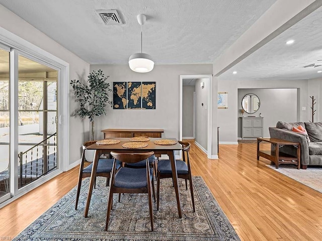 dining space with a textured ceiling, baseboards, visible vents, and light wood-style floors