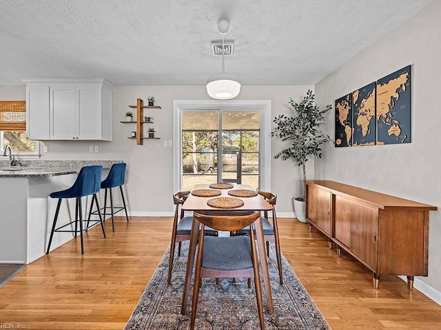 dining area featuring a healthy amount of sunlight, visible vents, a textured ceiling, and light wood finished floors