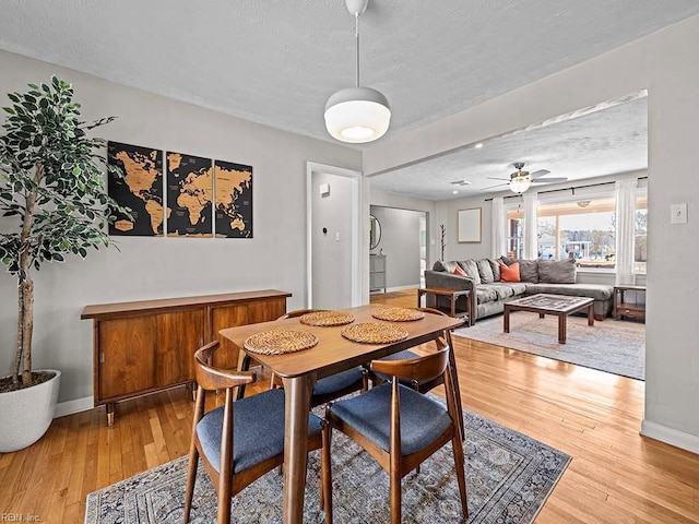 dining area featuring a textured ceiling, light wood-type flooring, a ceiling fan, and baseboards