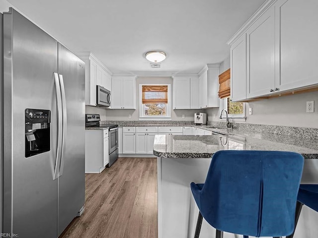 kitchen with stainless steel appliances, a peninsula, a sink, white cabinets, and light stone countertops