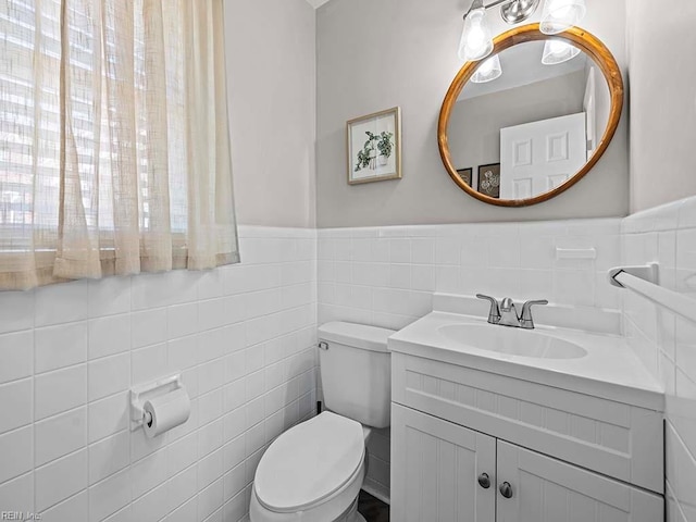 half bath featuring toilet, vanity, tile walls, and wainscoting