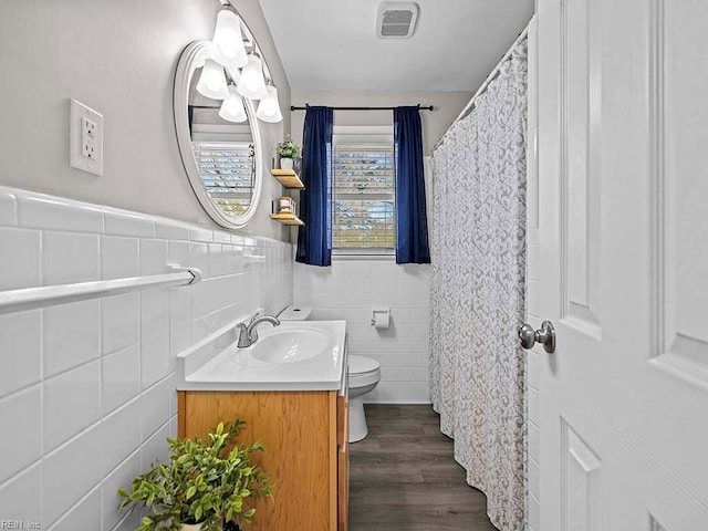 bathroom featuring visible vents, toilet, wood finished floors, vanity, and tile walls