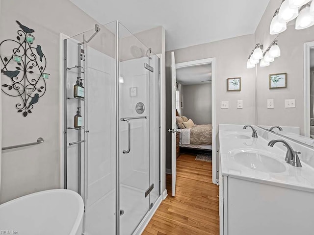 ensuite bathroom with a stall shower, a freestanding tub, a sink, and wood finished floors