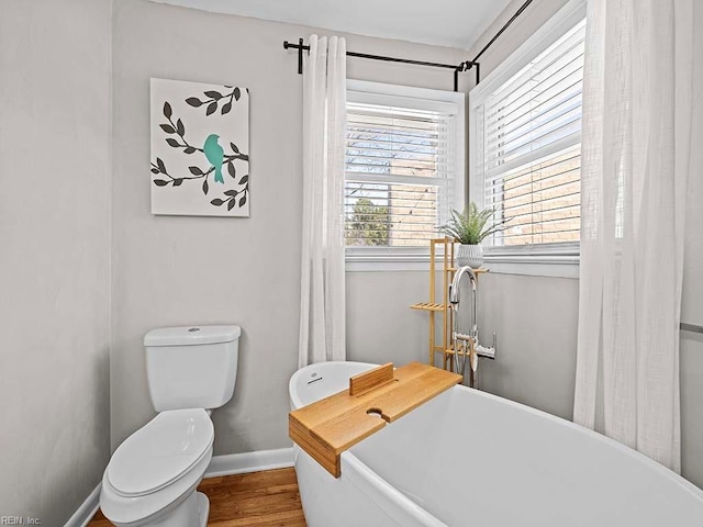 full bath featuring toilet, a soaking tub, baseboards, and wood finished floors