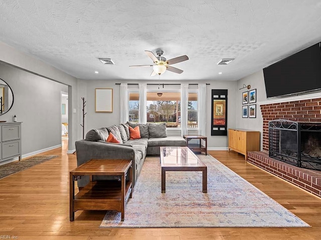 living room featuring a textured ceiling, a fireplace, wood finished floors, and visible vents