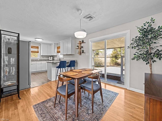 dining space featuring a textured ceiling, light wood-type flooring, visible vents, and baseboards