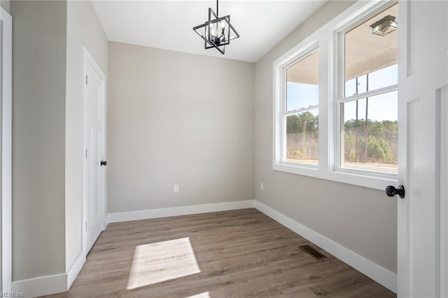 unfurnished room featuring visible vents, baseboards, a chandelier, and wood finished floors