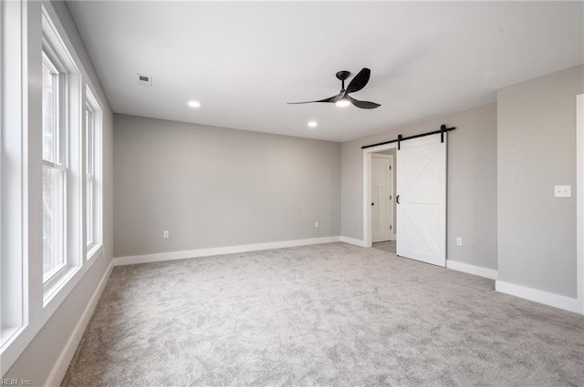 empty room with a barn door, visible vents, baseboards, carpet flooring, and recessed lighting