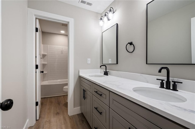 full bathroom with double vanity, visible vents, a sink, and wood finished floors