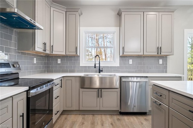 kitchen featuring stainless steel appliances, light countertops, light wood-style flooring, a sink, and extractor fan