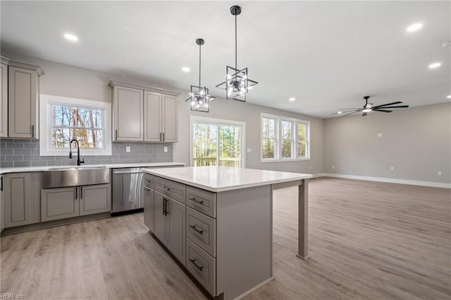 kitchen featuring a center island, gray cabinets, light countertops, stainless steel dishwasher, and a sink