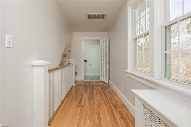 hall featuring an upstairs landing, visible vents, light wood-type flooring, and baseboards