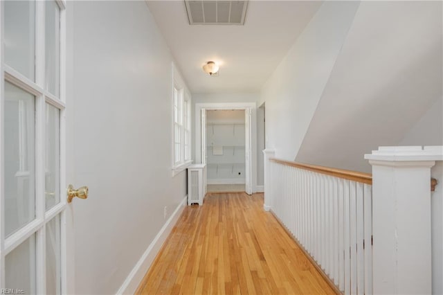 hall with visible vents, baseboards, and light wood finished floors