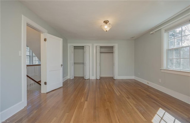 unfurnished bedroom featuring baseboards, multiple closets, and light wood-style floors