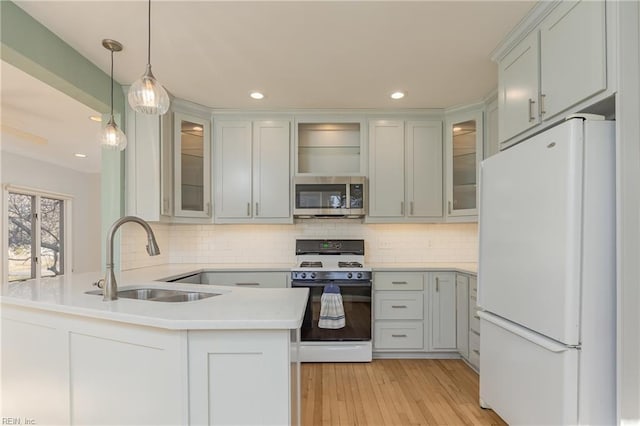 kitchen with a peninsula, freestanding refrigerator, a sink, gas range oven, and stainless steel microwave