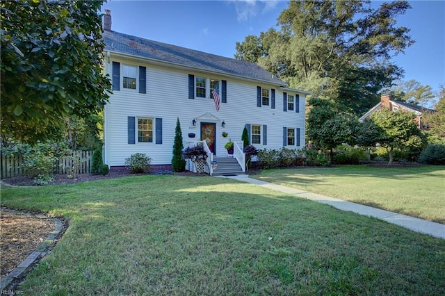 colonial home featuring a chimney, a front yard, and fence