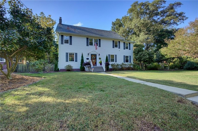 colonial inspired home with a chimney, a front lawn, and fence