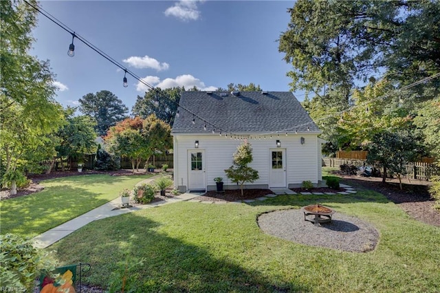 back of property featuring an outdoor fire pit, a lawn, a shingled roof, and fence