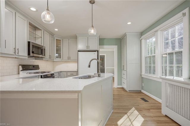 kitchen with a sink, decorative light fixtures, backsplash, white appliances, and light wood finished floors