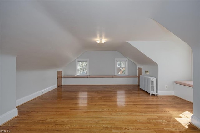 additional living space with light wood-type flooring, lofted ceiling, radiator, and baseboards