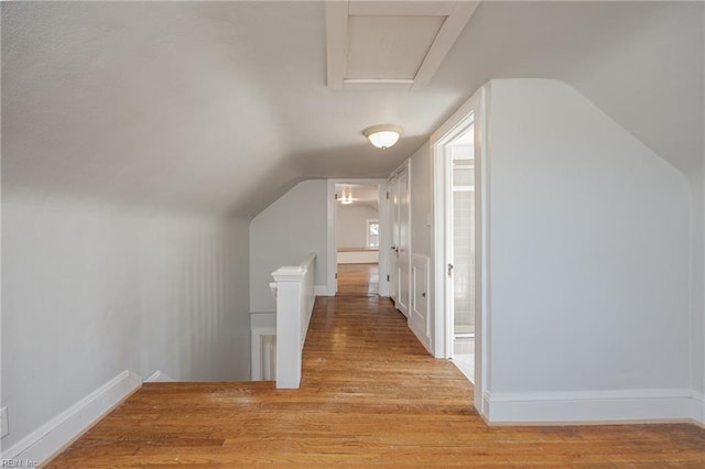 hall with an upstairs landing, baseboards, lofted ceiling, and wood finished floors